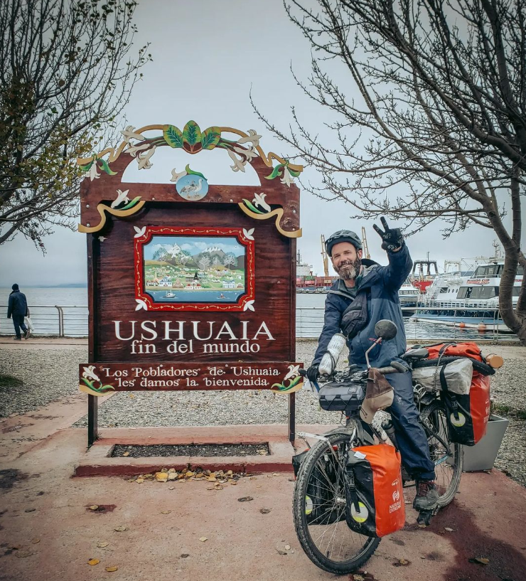 Foto do viajante cervejeiro em sua bicicleta, ao lado da placa de Ushuaia