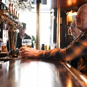 Foto de um homem mais velho, com camisa listrada, sentado no balcão de um pub sueco. Capa do post Mercado cervejeiro na Suécia